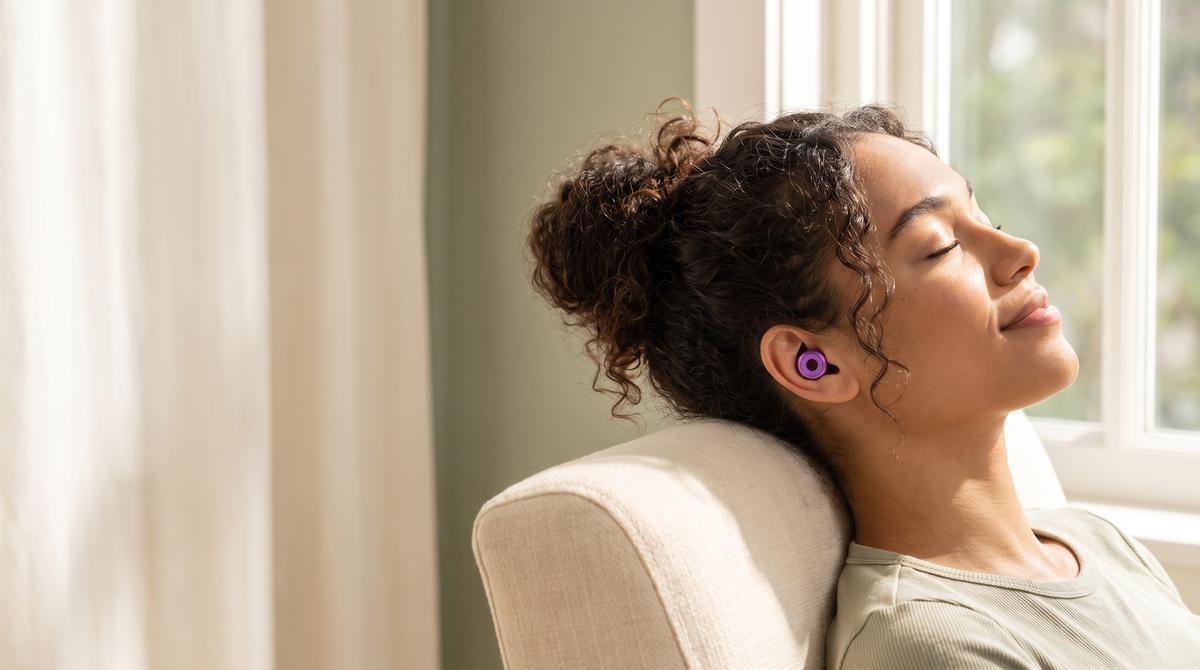 Woman relaxing in a sunlit armchair wearing a purple DAYBLIND ring earplug